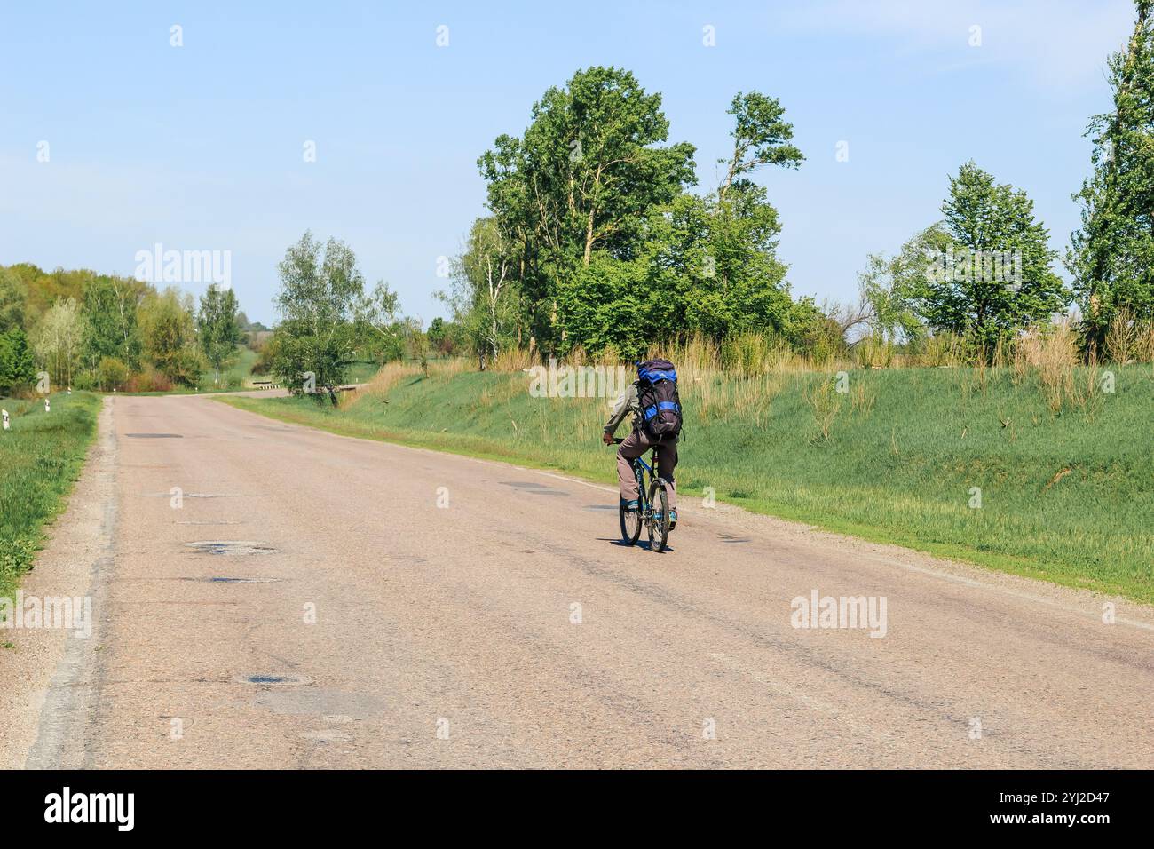 Un ciclista solitario con uno zaino cavalca una mountain bike in una giornata estiva di sole su un percorso ciclabile in autostrada. Foto di viaggio, attività estive. Foto Stock