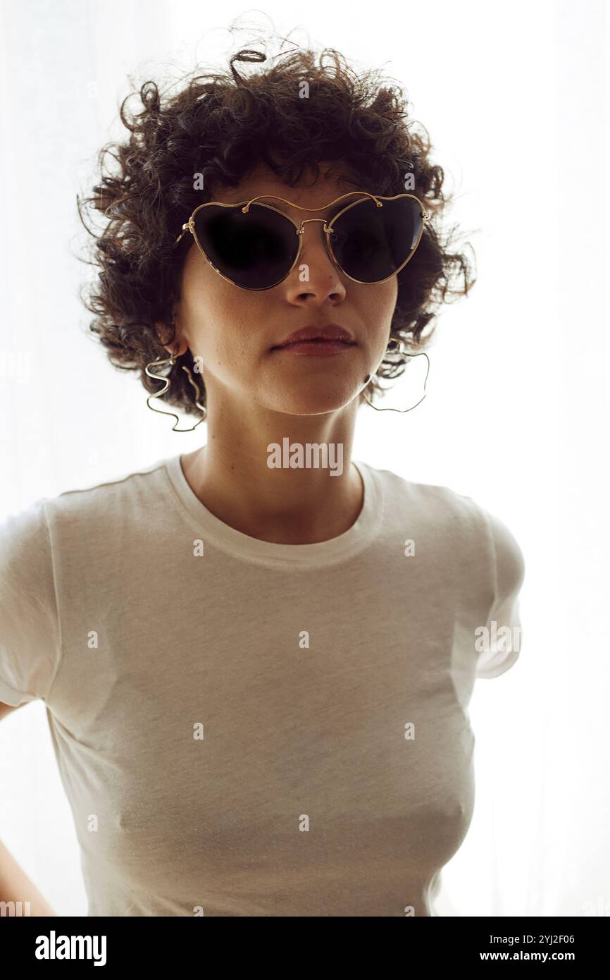 Donna con capelli ricci che indossa una t-shirt bianca e occhiali da sole Foto Stock