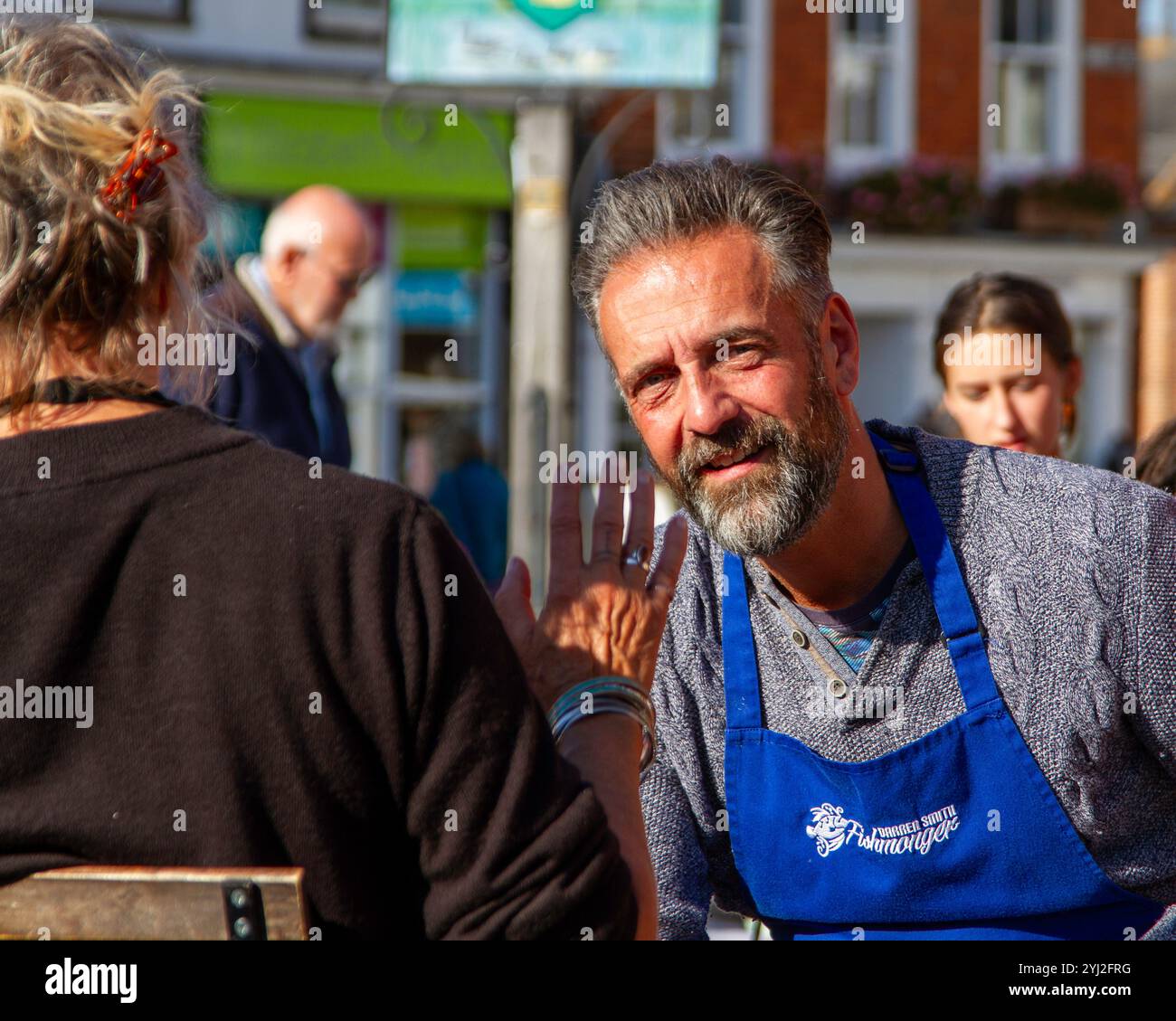 Ben curato, abbronzato e seduto sul mercato che commerciava pescivendolo in pausa si piega in avanti prestando attenzione e ascoltando una donna che gestiva con la mano. Foto Stock