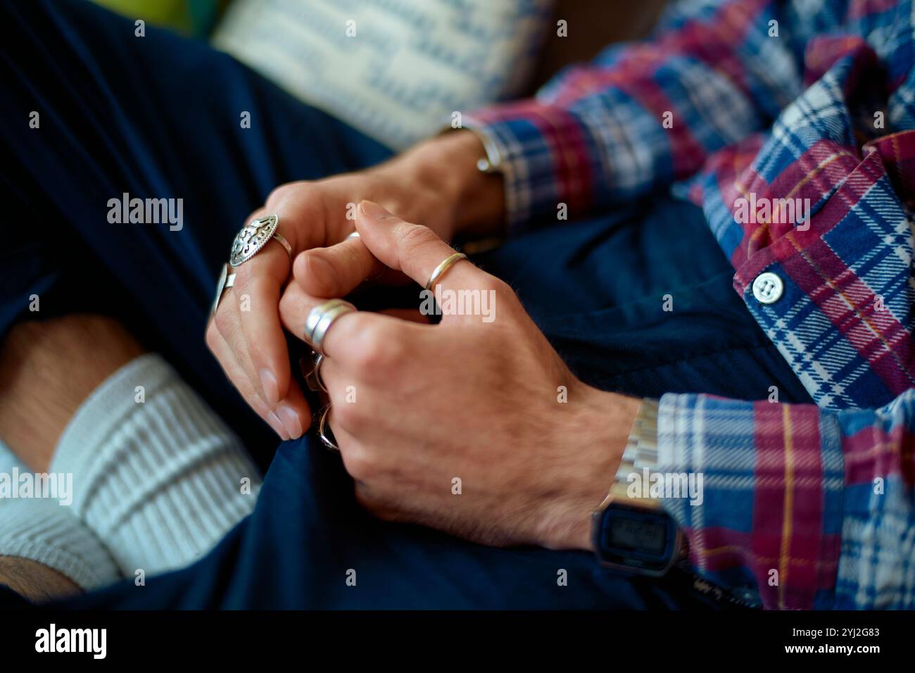 Primo piano di un uomo con le mani chiuse che indossa anelli d'argento, camicia a scacchi, calze bianche e jeans. Foto Stock