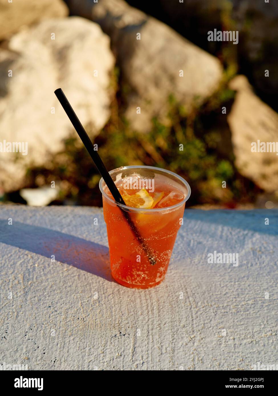 Un cocktail rinfrescante in una tazza di plastica con una paglia e una fetta di agrumi, seduti in cima a una rustica superficie di pietra sotto la luce del sole, Napoli, Italia Foto Stock