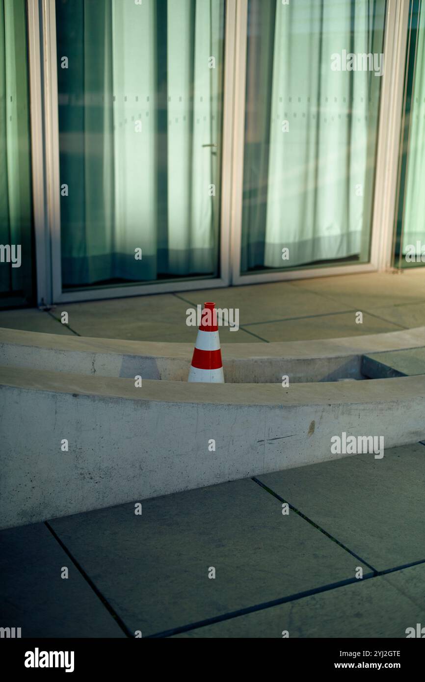 Il cono segnaletico rosso e bianco si trova su una sporgenza di cemento di fronte a un edificio in vetro, Berlino, Germania Foto Stock