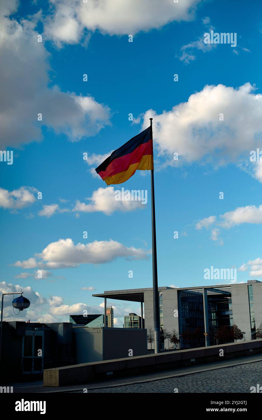 Una bandiera tedesca sventola nella brezza sullo sfondo di cielo blu e nuvole sparse, con edifici moderni in lontananza, Berlino, Germania Foto Stock