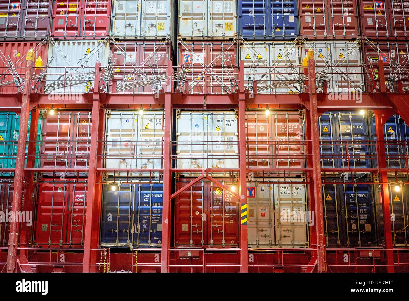Lavoratore che ispeziona una grande pila di container rossi su una nave da carico di notte con un riflettore che illumina la scena. Foto Stock