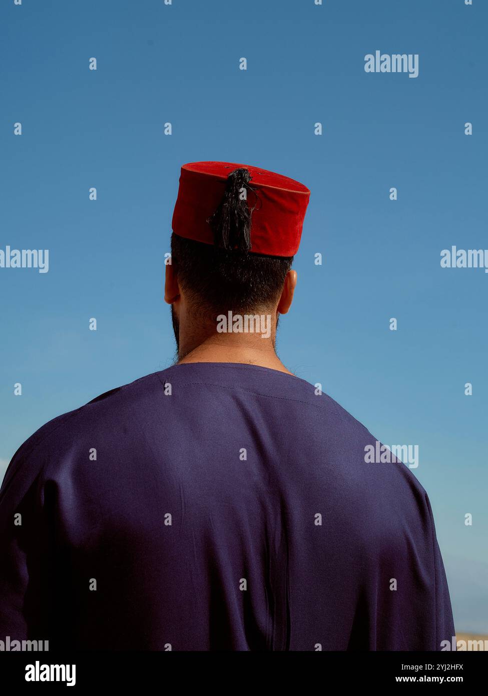 L'uomo in abbigliamento tradizionale con un cappello rosso di fez si erge sullo sfondo di un cielo blu, il Marocco Foto Stock