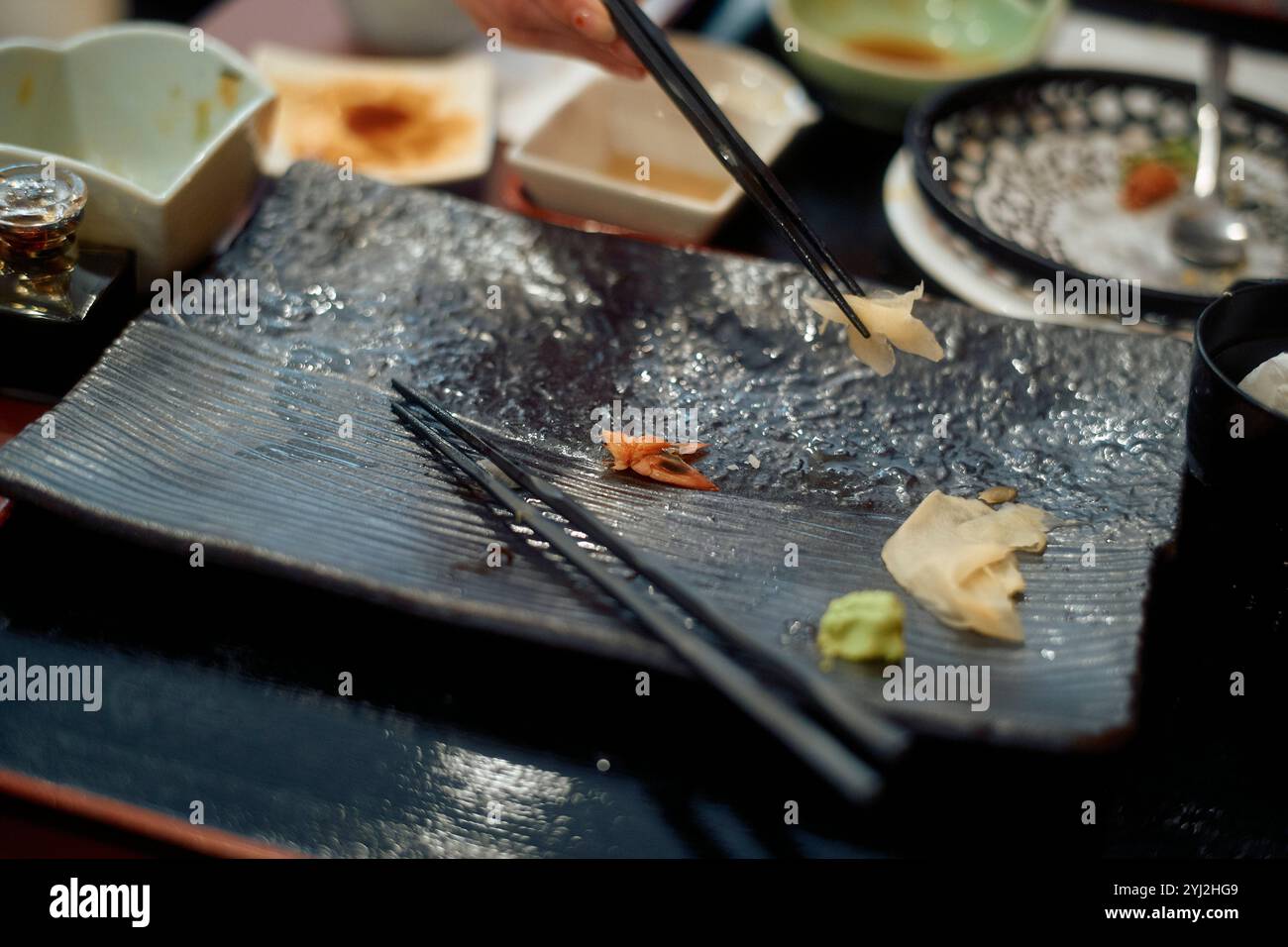 Primo piano di un piatto di sushi disordinato con bacchette e resti di un pasto su un piatto scuro e ruvido. Foto Stock