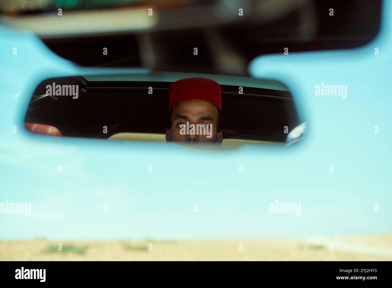 Uomo con cappello rosso riflesso nello specchietto retrovisore di un'auto, Marocco Foto Stock