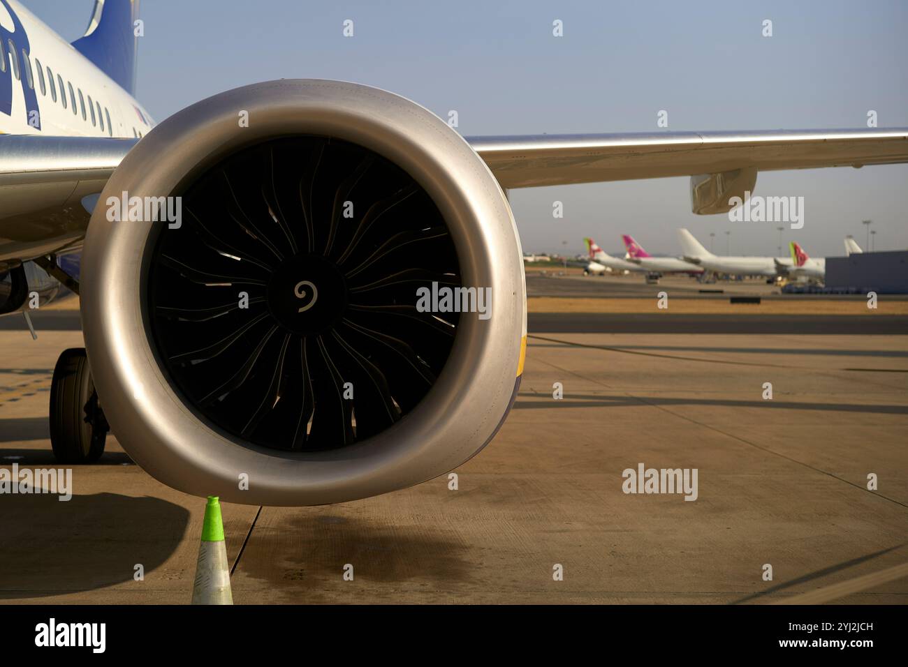 Vista ravvicinata di un motore a reazione su un aereo in aeroporto con altri aerei sullo sfondo in una giornata limpida. Foto Stock