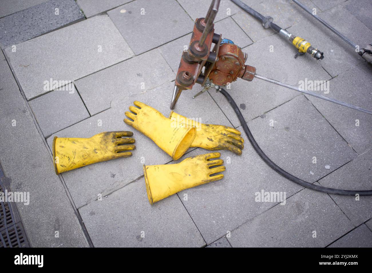 I guanti in gomma gialli poggiano su un marciapiede cittadino accanto a attrezzi, macchinari e attrezzature pesanti Foto Stock