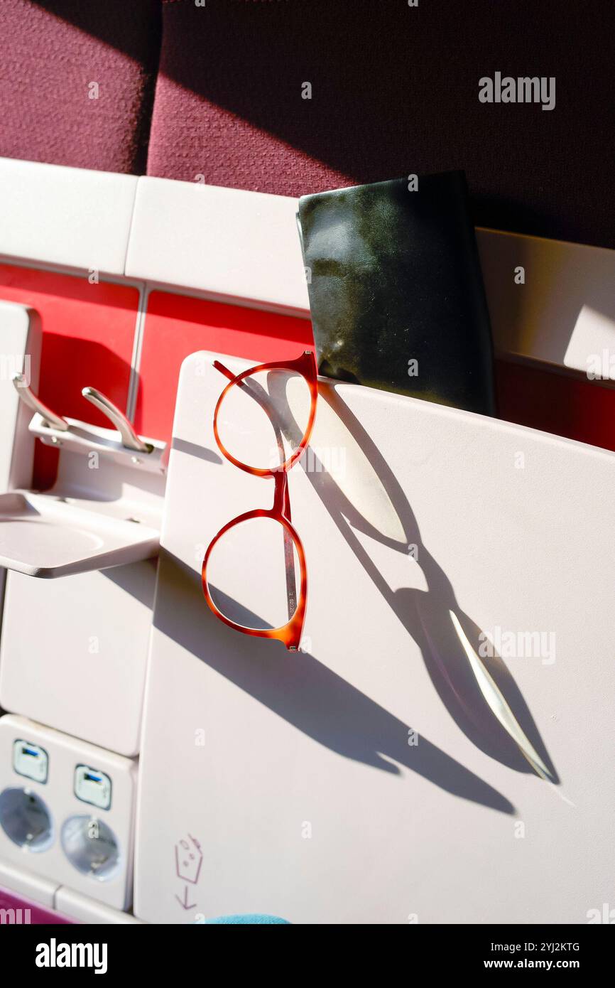 Vetri rossi che proiettano un'ombra su un vassoio bianco aperto su uno sfondo rosso e bianco in una fila di posti a sedere in treno Foto Stock