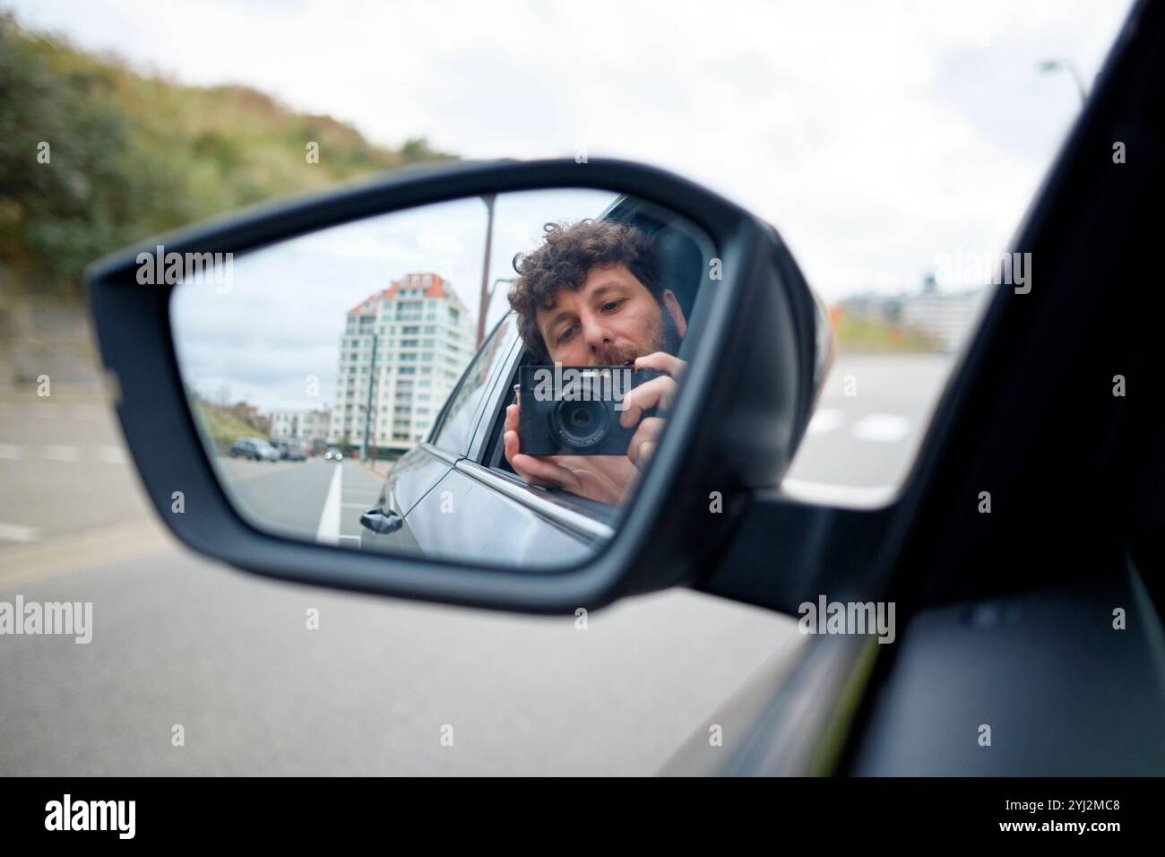 Una persona scatta una foto di se stessa nello specchio laterale di un'auto su uno sfondo urbano, il Belgio Foto Stock