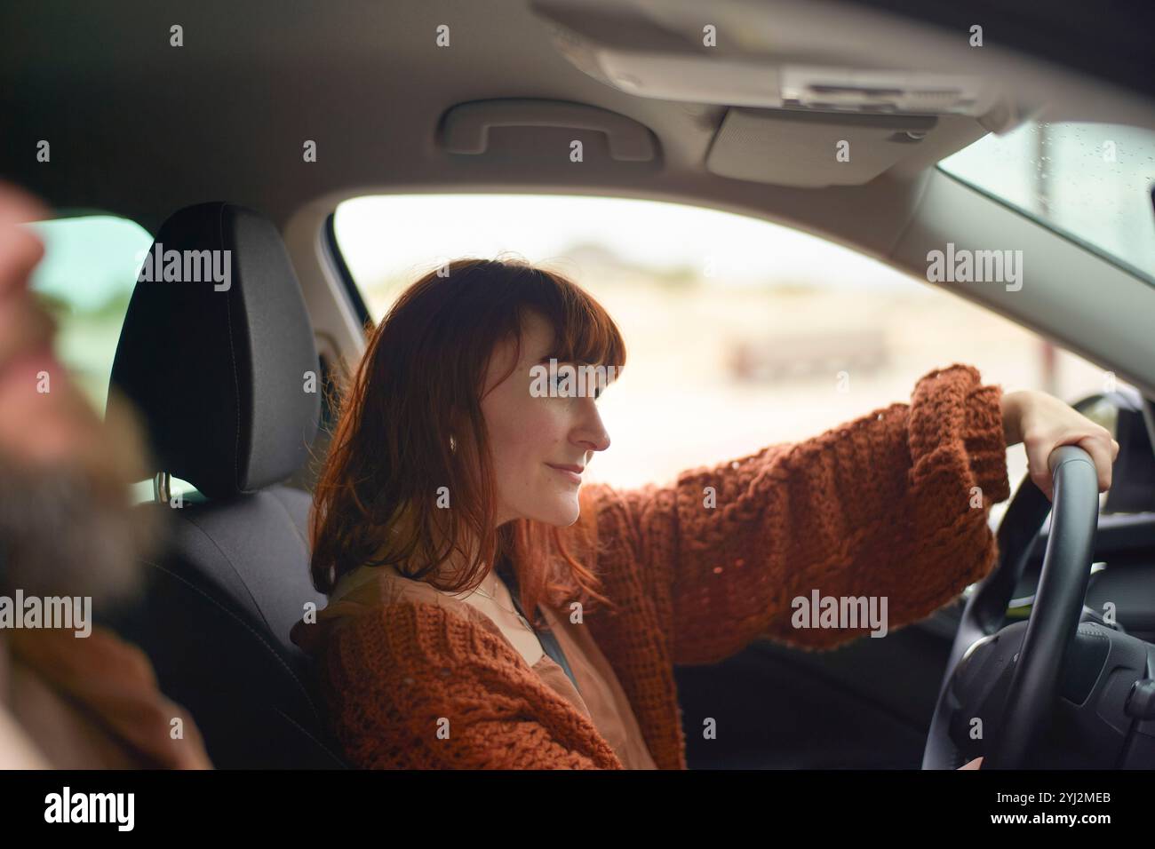 Una donna sorridente alla guida di un'auto, che guarda le spalle con un passeggero in primo piano. Foto Stock