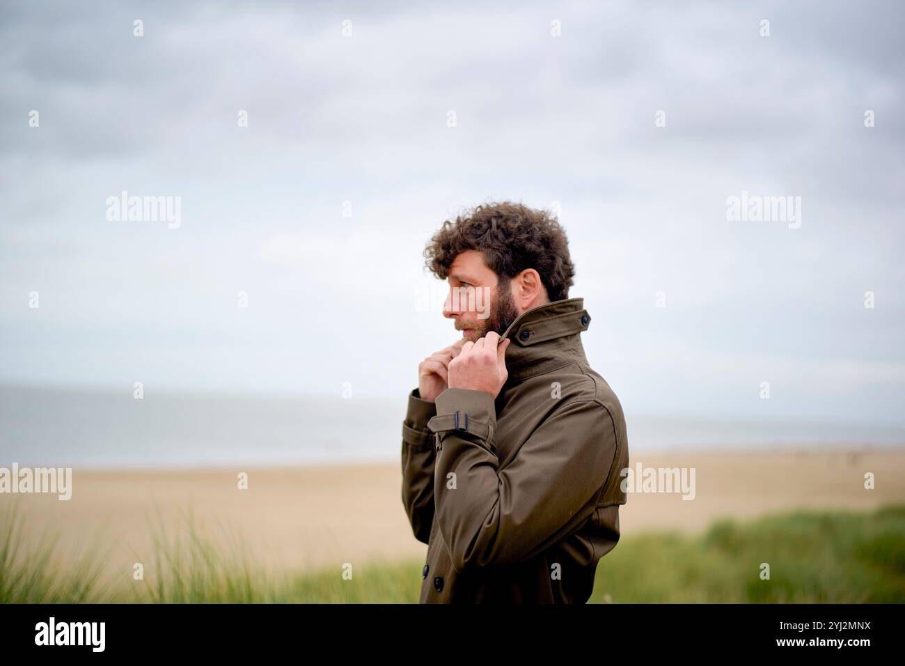 Uomo in una giacca che contempla in una giornata fredda in spiaggia con cieli ricoperti, Belgio Foto Stock