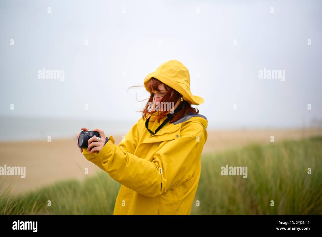 Donna in impermeabile giallo che guarda la macchina fotografica in una giornata di spiaggia nuvolosa, Belgio Foto Stock