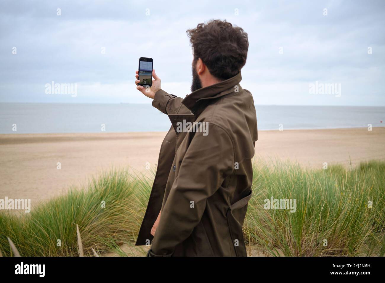 Uomo che scatta una foto del mare con il suo smartphone dalle dune della spiaggia, in Belgio Foto Stock