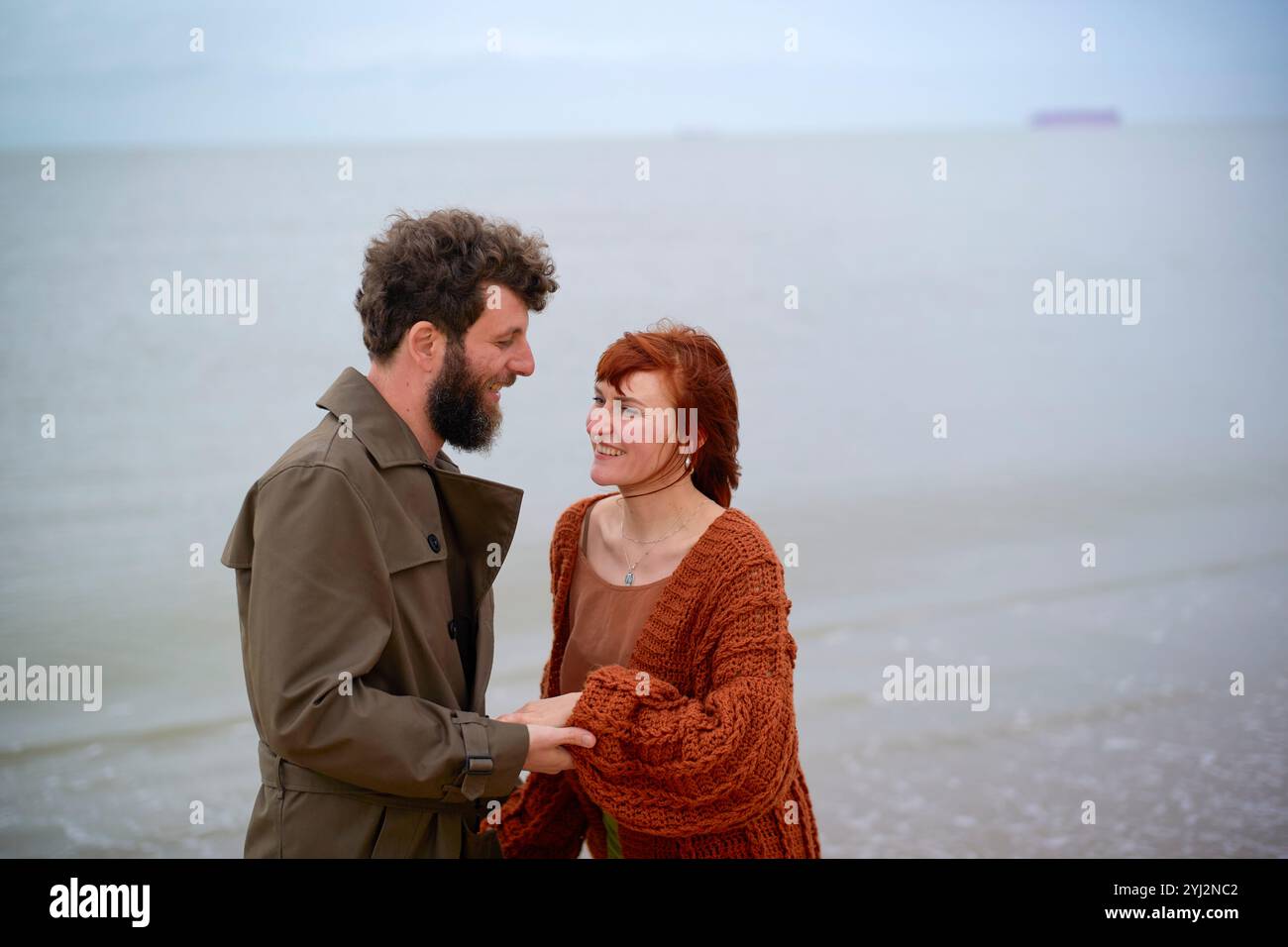 Una coppia si sorride in una giornata nuvolosa in spiaggia, con l'oceano e una nave sullo sfondo, il Belgio Foto Stock