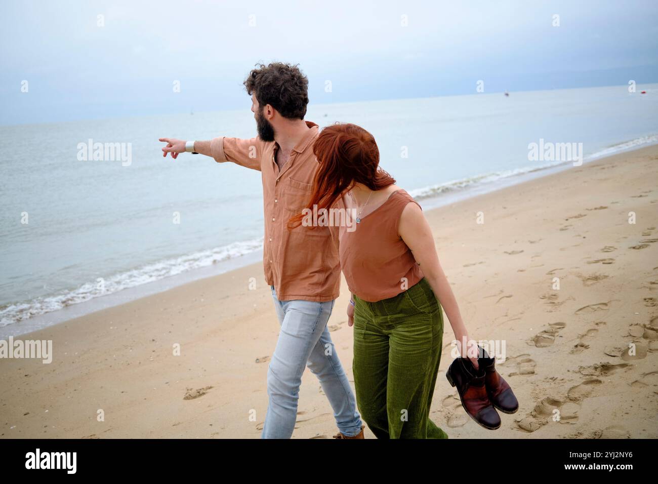 Un uomo e una donna che camminano a piedi nudi su una spiaggia sabbiosa, con l'uomo che punta verso il mare, in Belgio Foto Stock