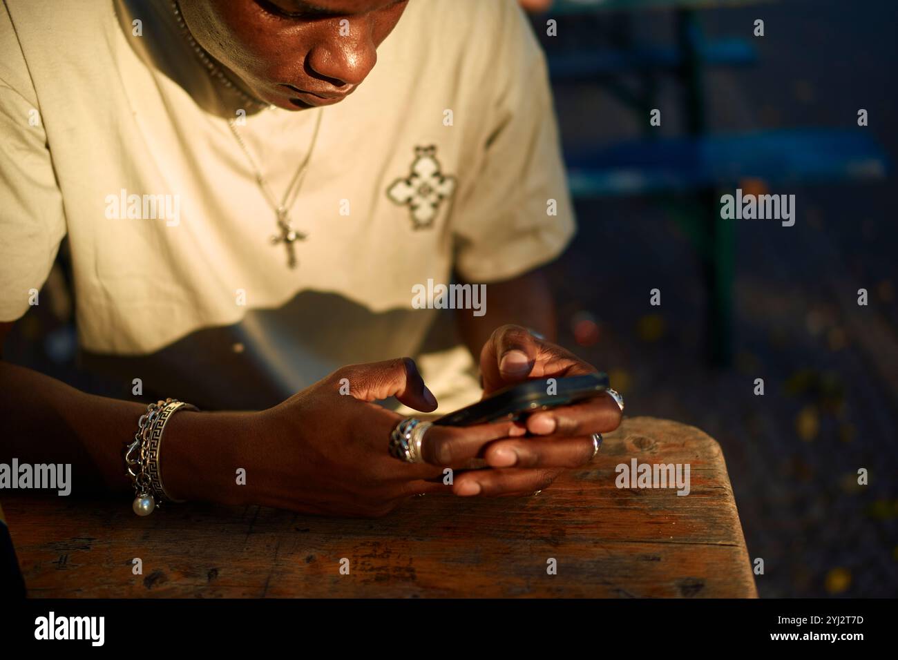 Giovane uomo adulto concentrato sul suo smartphone a un tavolo all'aperto illuminato dal sole, Berlino, Germania Foto Stock