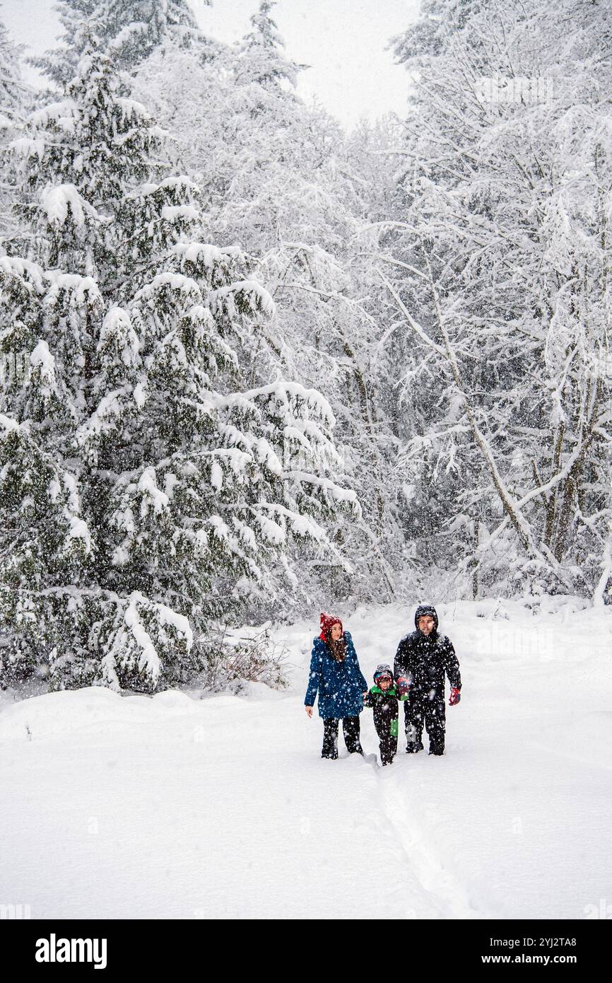 Una famiglia che si gode una passeggiata invernale tra alberi innevati. Foto Stock