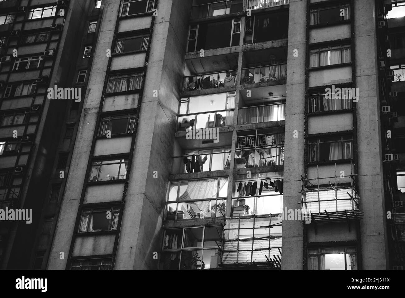 Le finestre degli edifici residenziali di Hong Kong mostrano calore serale, con interni illuminati e abiti appesi. Foto Stock