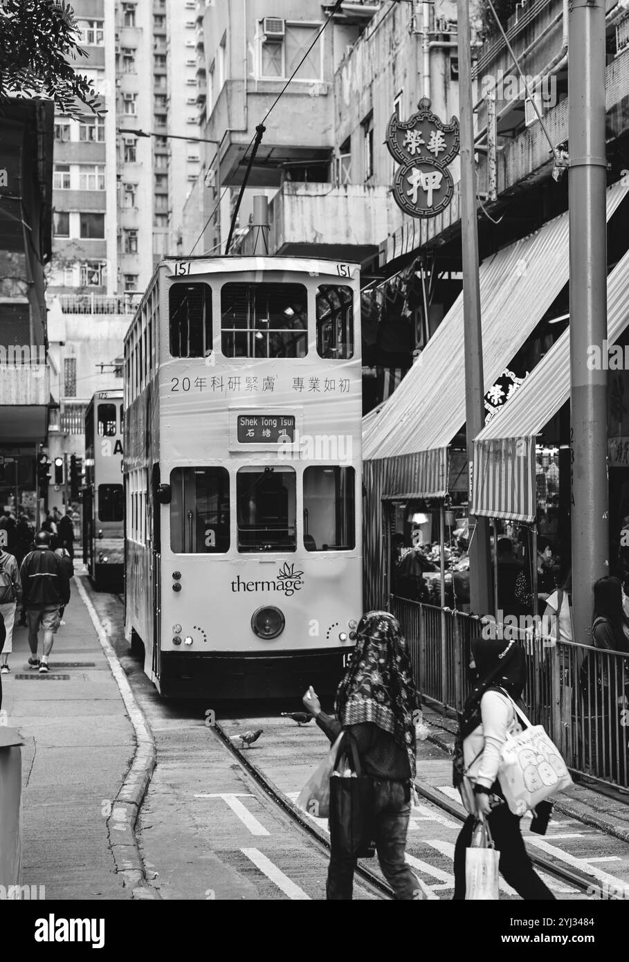 Un classico tram scivola attraverso la stazione del mercato di Hong Kong mentre i pedoni percorrono le vivaci strade piene di negozi e attività. Foto Stock