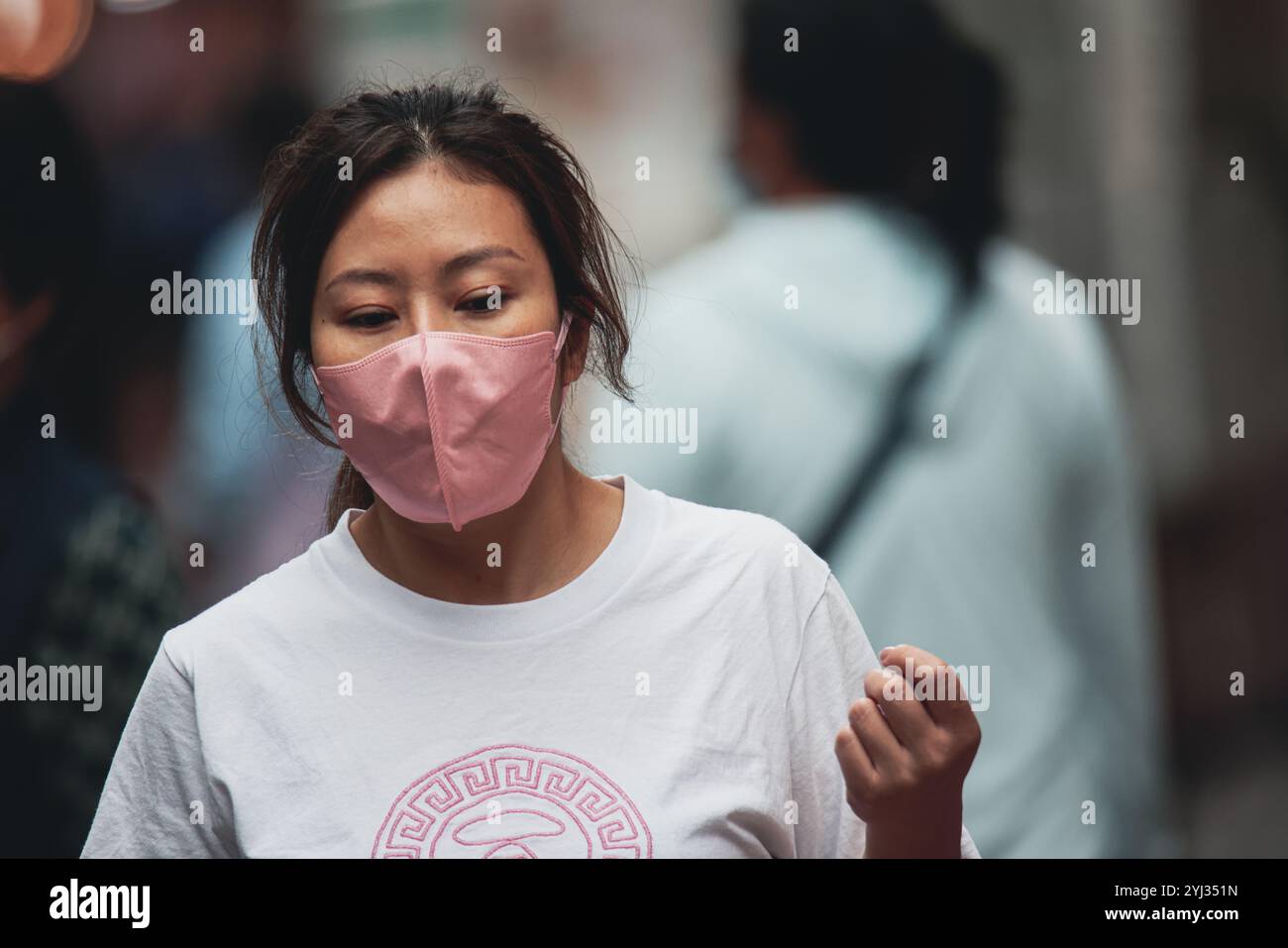 Una giovane donna con una maschera rosa passeggia per una strada vivace, circondata da gente e vivace vita urbana nel centro di Hong Kong. Foto Stock