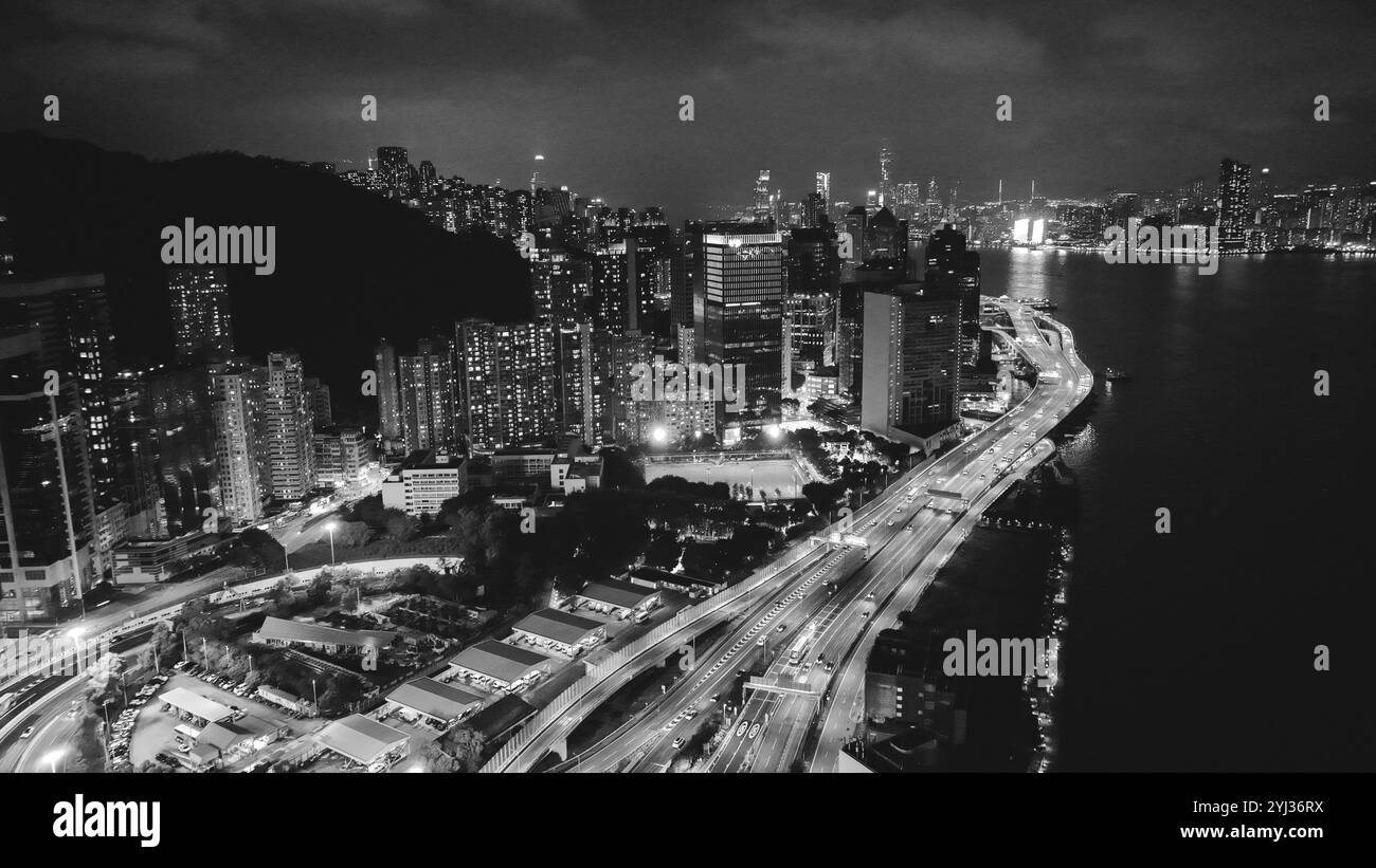 Il vibrante skyline di Hong Kong illumina la notte, mostrando alti edifici e lo scintillante lungomare lungo la trafficata costa. Foto Stock