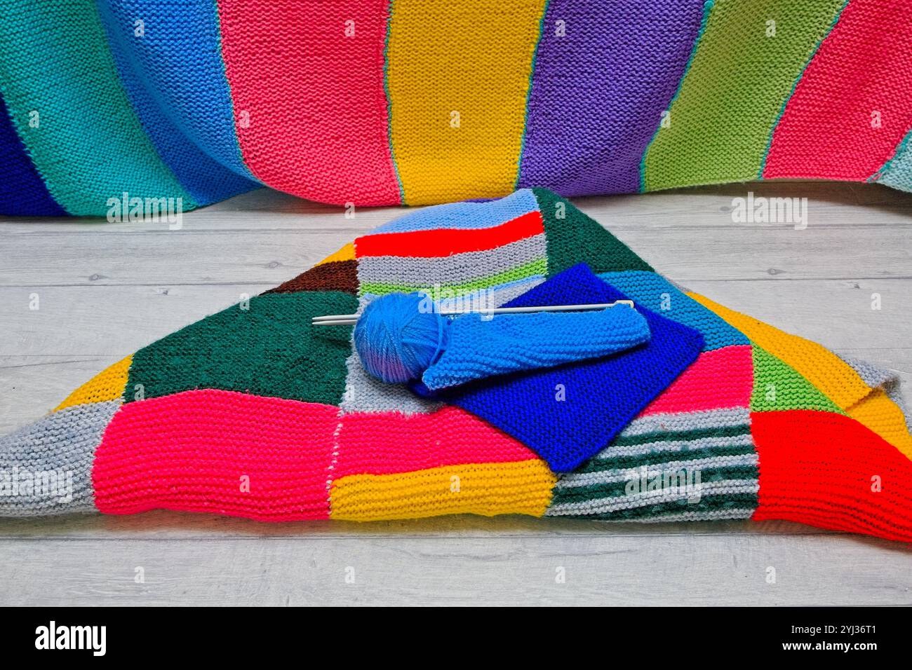 Guardando verso il basso su una palla blu di lana con aghi per maglieria posti su una coperta a maglia di patchwork Foto Stock