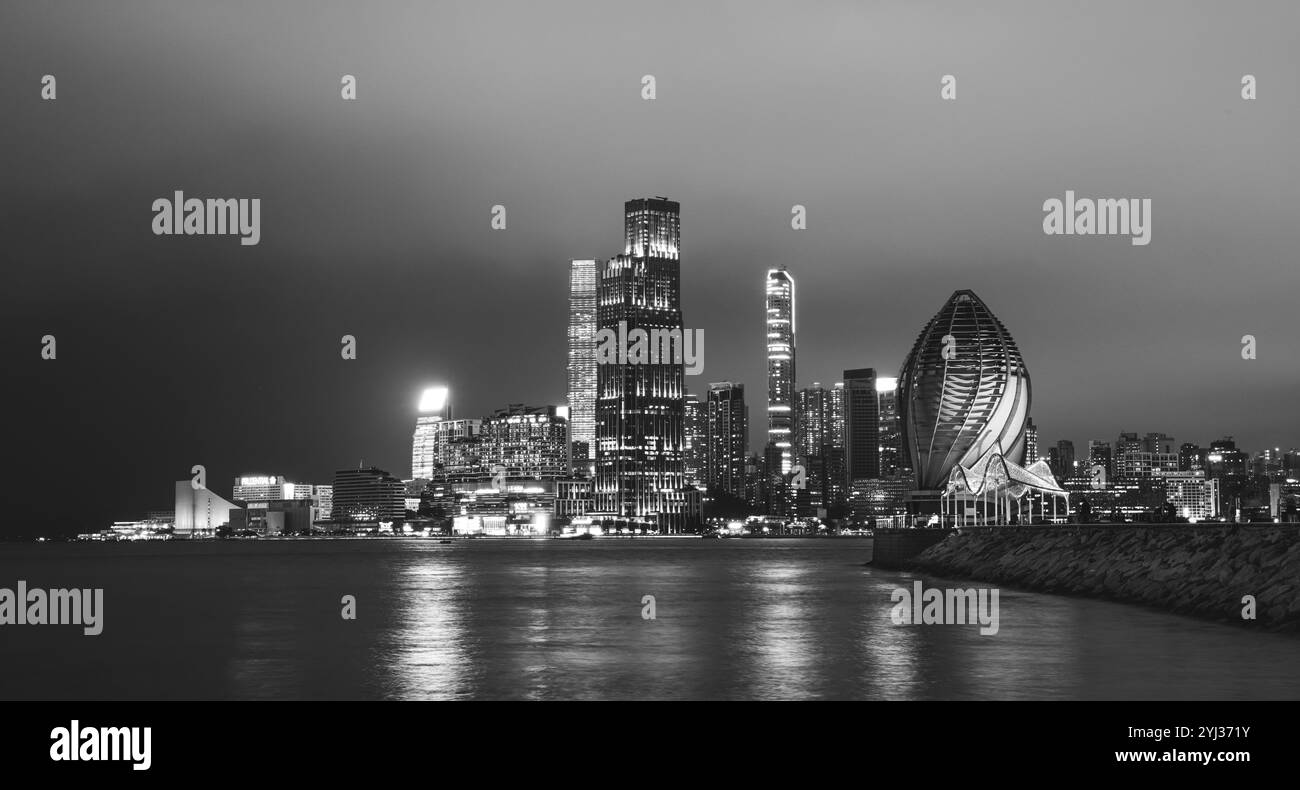 Un'abbagliante esposizione dello skyline di Hong Kong illumina la notte con edifici torreggianti che riflettono su acque calme. Foto Stock