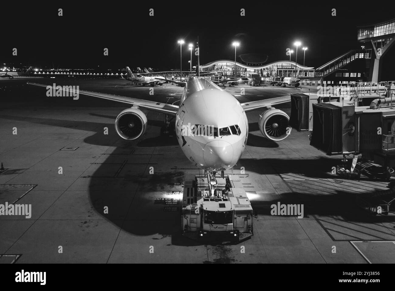 Un aereo viene servito di notte all'aeroporto di Hong Kong, con il terminal illuminato e un equipaggio di terra che si prepara per il volo successivo. Foto Stock