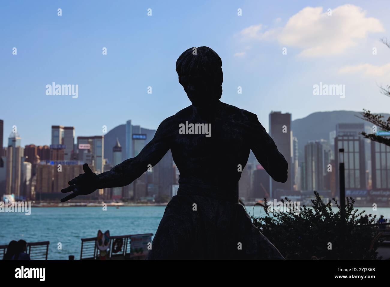 La statua di Bruce Lee si erge in una posa dinamica sul lungomare, con lo skyline e il porto di Hong Kong visibili sullo sfondo. Foto Stock