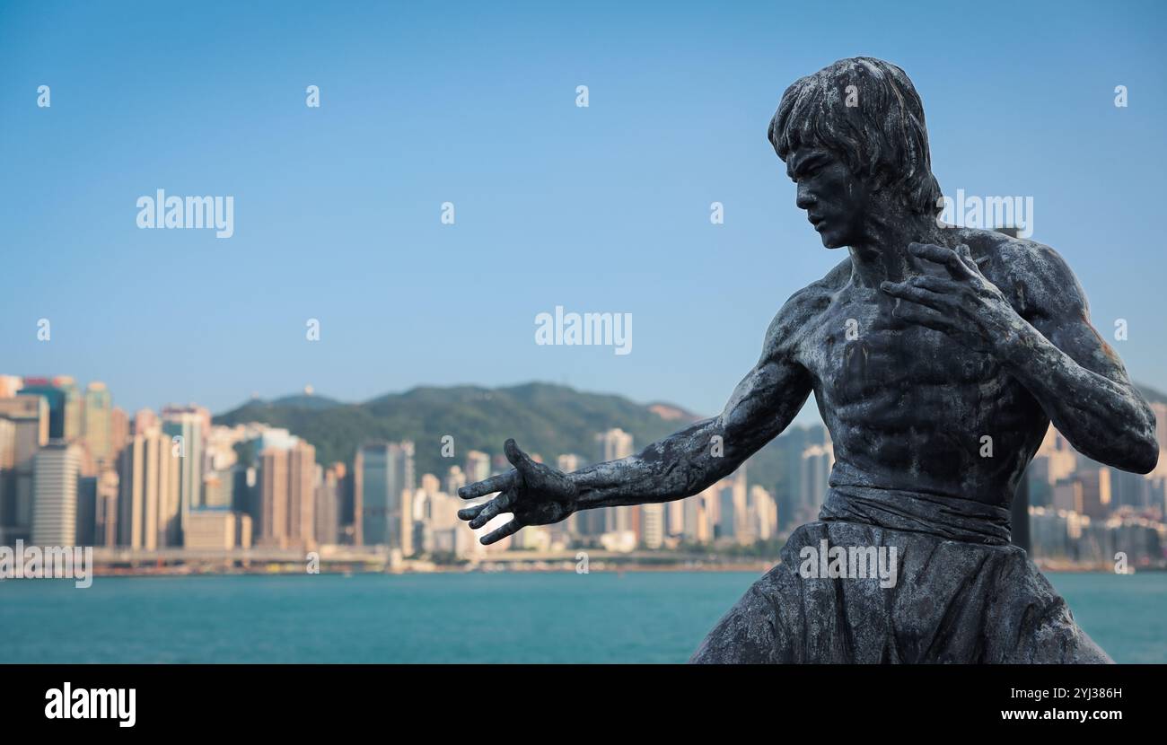 Una dettagliata statua di Bruce Lee si affaccia sul porto, con il dinamico skyline di Hong Kong che torreggia in lontananza. Foto Stock