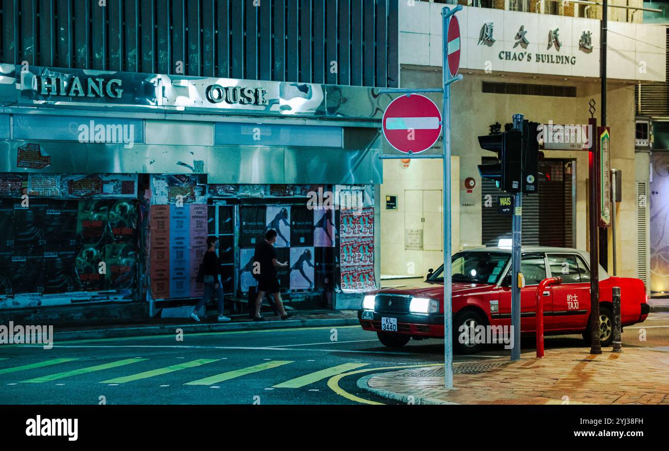 Un taxi luminoso naviga in una vivace strada di Hong Kong illuminata da luci al neon sotto il cielo notturno. Foto Stock