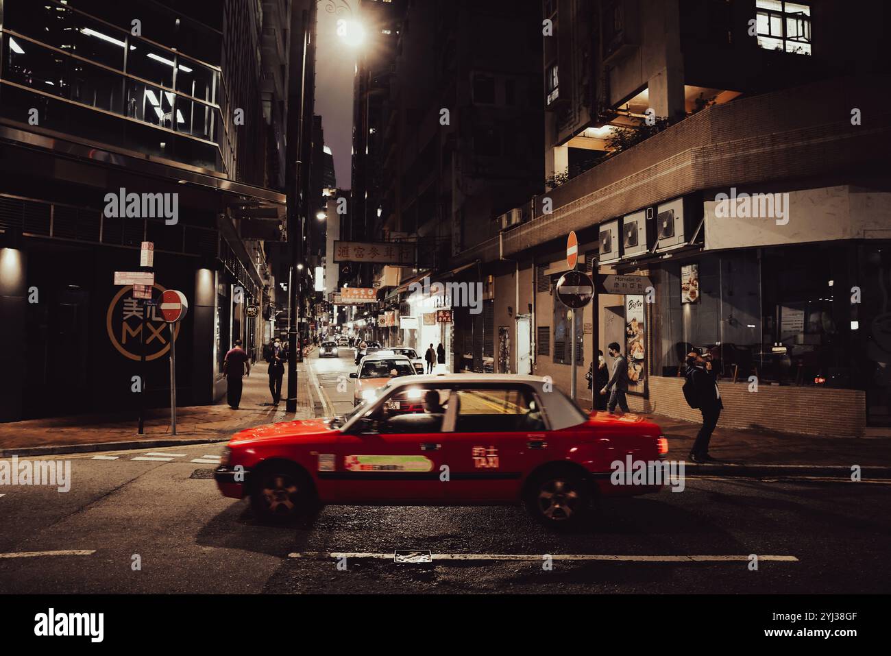 Un taxi rosso percorre una tranquilla strada di Hong Kong illuminata dalle luci della città dopo il tramonto. Foto Stock