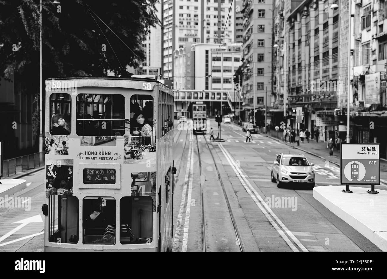 Un vibrante tram si muove lungo il tram circondato da alti edifici e da un'atmosfera frenetica della città di Hong Kong. Foto Stock