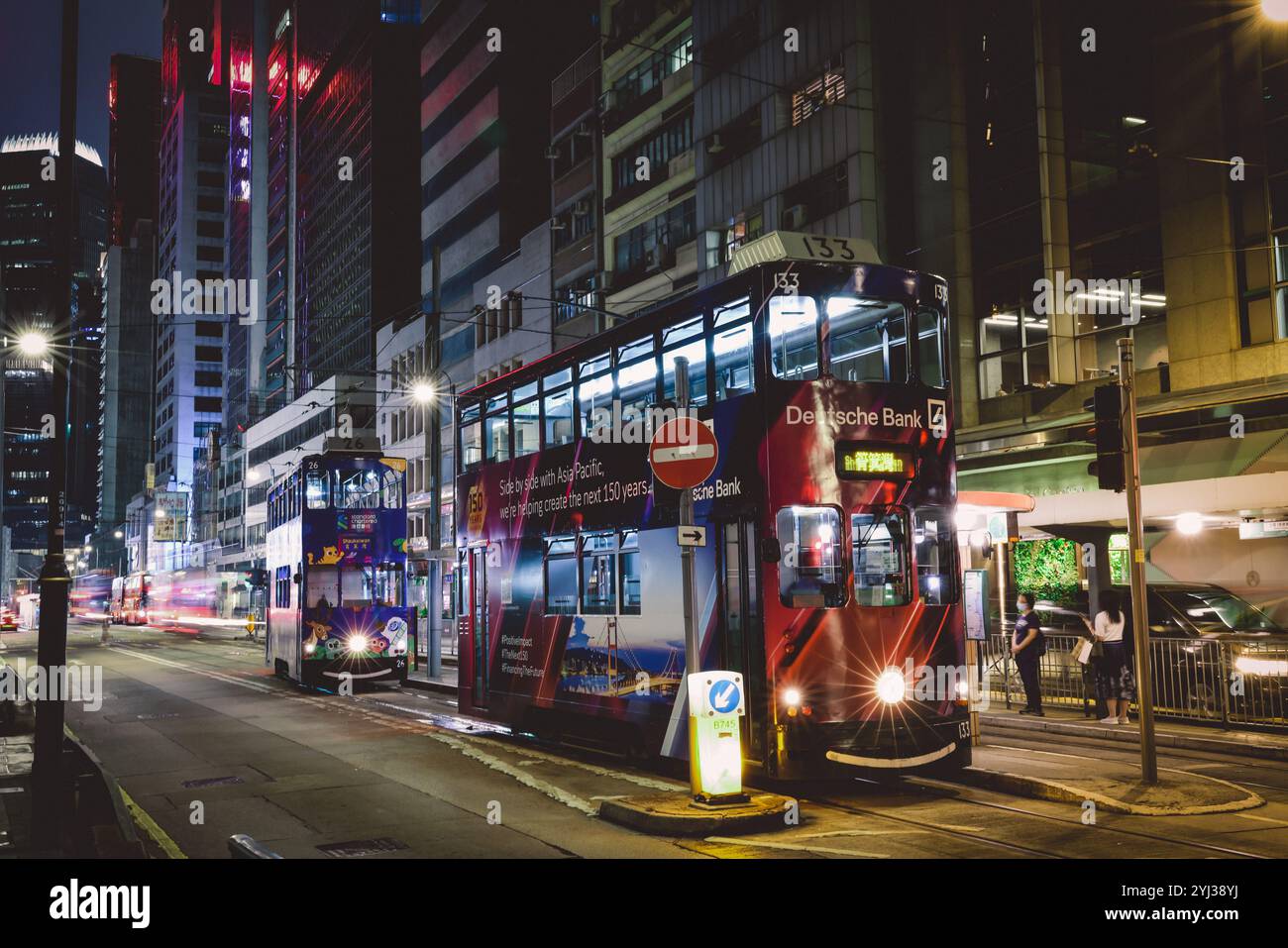 Un tram a due piani opera nel vibrante paesaggio urbano di Hong Kong, illuminato da colorate luci al neon di sera. Foto Stock