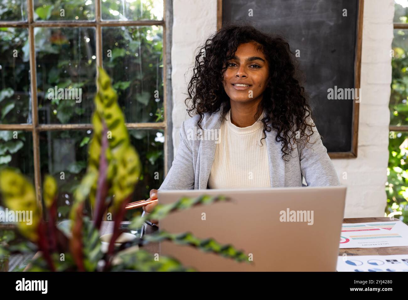 Donna sorridente che lavora con un laptop in ufficio a casa con piante intorno Foto Stock