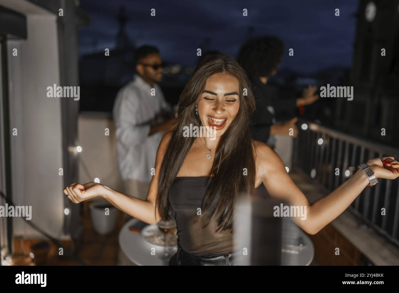 Donna felice che balla durante la festa serale sul tetto della città festeggiando con amici multietnici Foto Stock