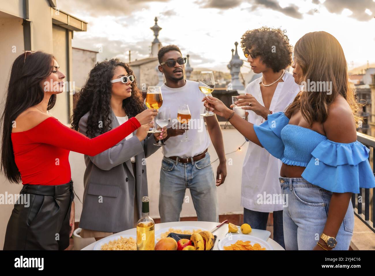 Amici multietnici brindano alla festa serale sul tetto della città Foto Stock