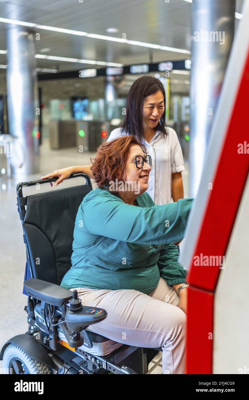 Foto con vista laterale verticale di una donna disabile e di un amico che acquistano il biglietto per la metropolitana Foto Stock