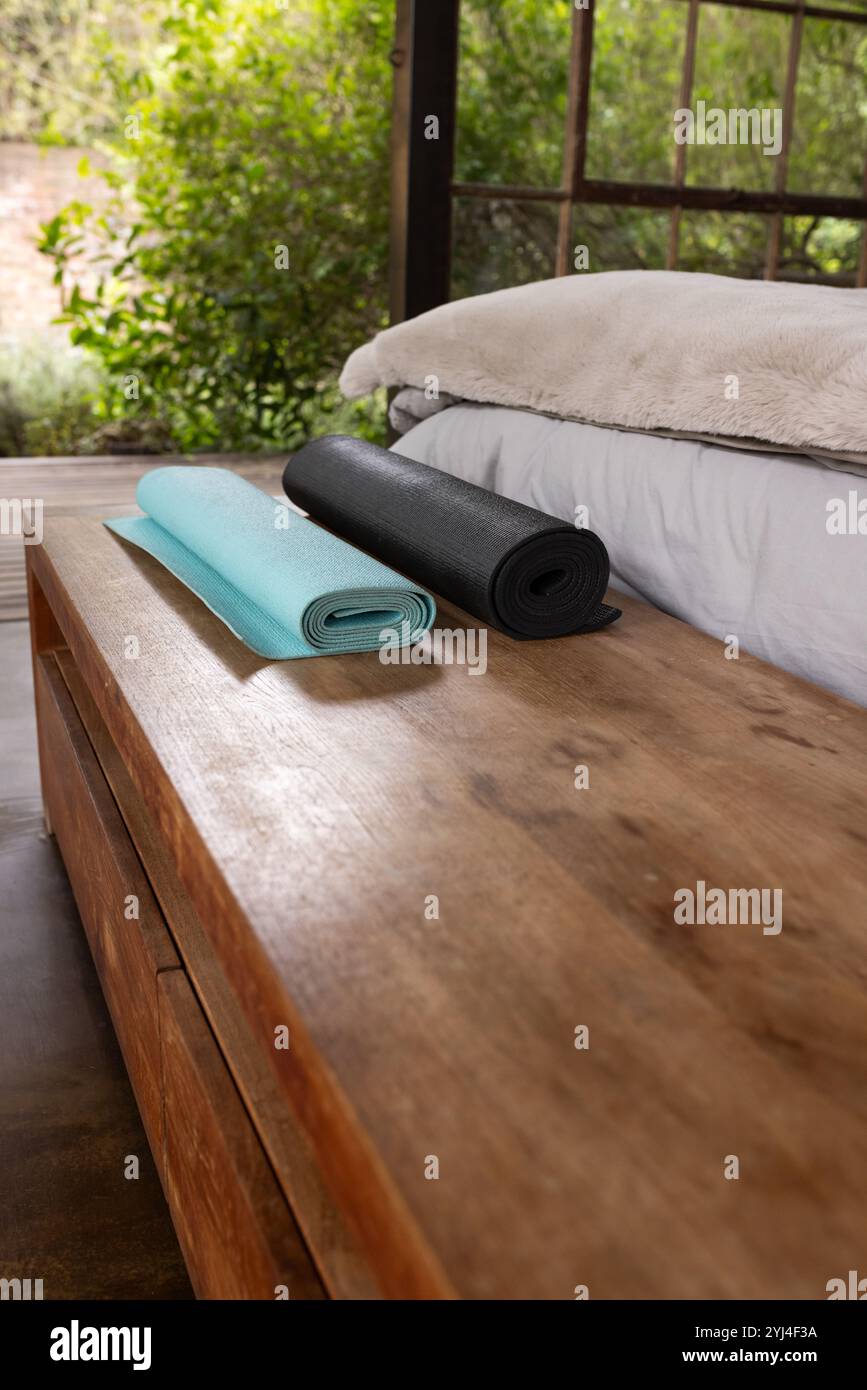 Stuoie da yoga arrotolate su panca di legno in un ambiente tranquillo Foto Stock