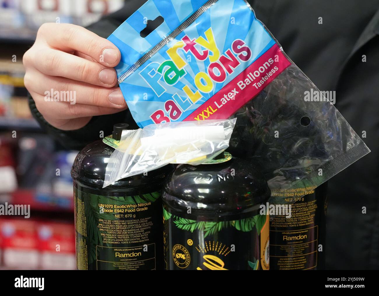 Amburgo, Germania. 13 novembre 2024. ILLUSTRAZIONE - un dipendente tiene un sacchetto di palloncini accanto a tre lattine di gas ridendo e un boccaglio (bianco) al bancone di un chiosco. L'uso di gas ridendo come droga da festa, soprattutto da parte dei giovani, potrebbe presto essere vietato in Germania. Il governo federale ha approvato un progetto del ministro della salute Lauterbach (SPD), che prevede anche un divieto di distribuzione tramite distributori automatici e negozi notturni. Crediti: Marcus Brandt/dpa/Alamy Live News Foto Stock