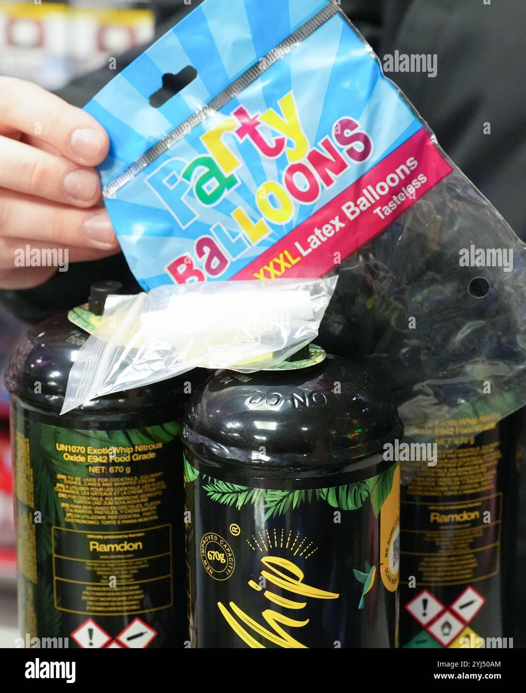 Amburgo, Germania. 13 novembre 2024. ILLUSTRAZIONE - un dipendente tiene un sacchetto di palloncini accanto a tre lattine di gas ridendo e un boccaglio (bianco) al bancone di un chiosco. L'uso di gas ridendo come droga da festa, soprattutto tra i giovani, potrebbe presto essere vietato in Germania. Il governo federale ha approvato un progetto del ministro della salute Lauterbach (SPD), che prevede anche un divieto di distribuzione tramite distributori automatici e negozi notturni. Crediti: Marcus Brandt/dpa/Alamy Live News Foto Stock