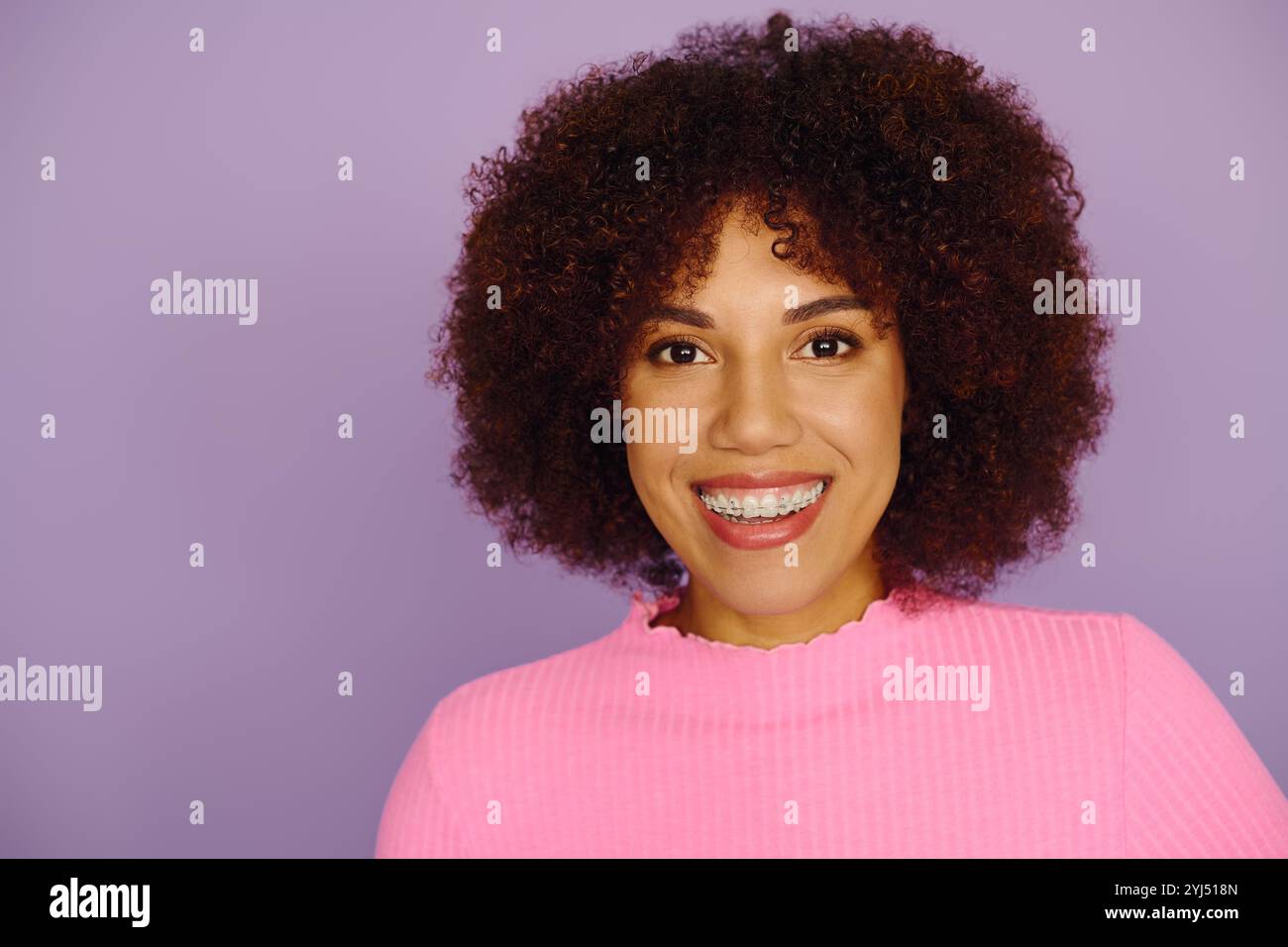 Una giovane donna afro-americana in abbigliamento casual rosa irradia gioia e fiducia in uno sfondo vivace. Foto Stock