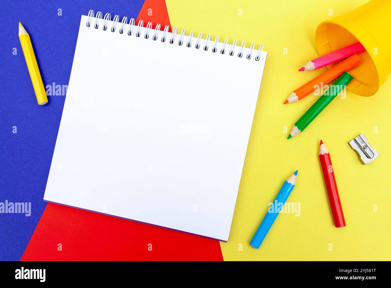Blocco note vuoto, matite a colori e una nitidezza su uno sfondo di carta a colori. Strumenti di disegno. Materiale didattico e per il tempo libero dei bambini. Foto Stock
