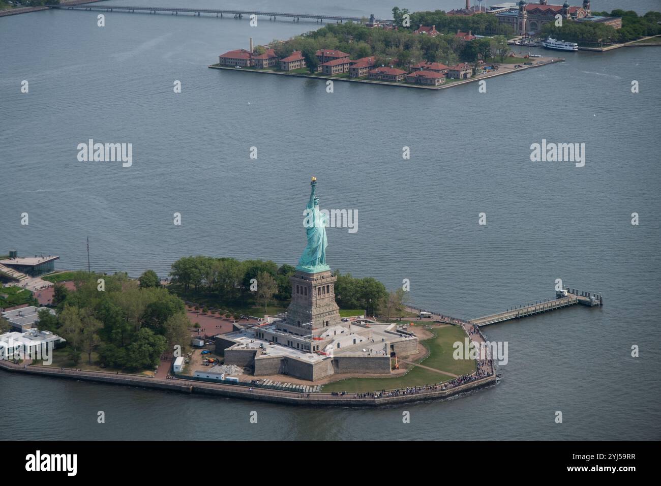 Statua della libertà su Liberty Island con Ellis Island sullo sfondo. Monumento storico circondato dalle acque del porto di New York e dai sentieri turistici. Foto Stock
