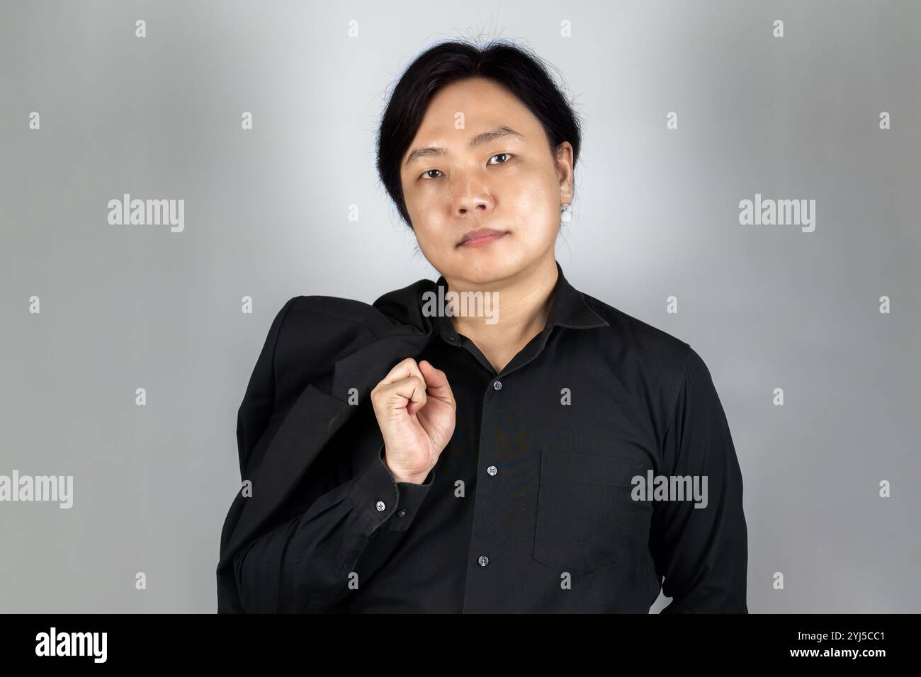 Il ritratto di un giovane asiatico che indossa la tuta nera ordinata con un'espressione semplice sullo sfondo bianco grigio scattato in studio. Foto Stock