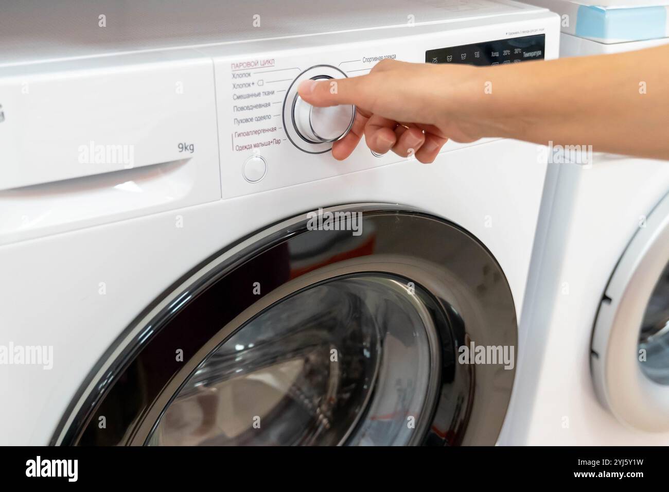 Una mano raggiunge per selezionare un ciclo di lavaggio sulla lavatrice. Foto Stock