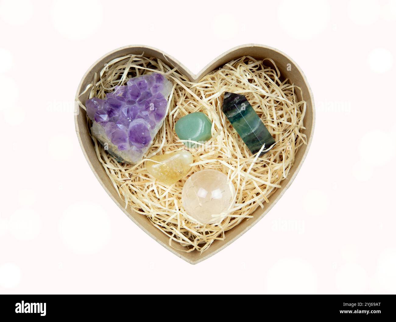 Vista dall'alto della scatola regalo a forma di cuore aperta con strisce di legno triturate - riempitivo per scatole regalo e pietre semi-preziose all'interno. Concetto di dono di guarigione spirituale. Foto Stock