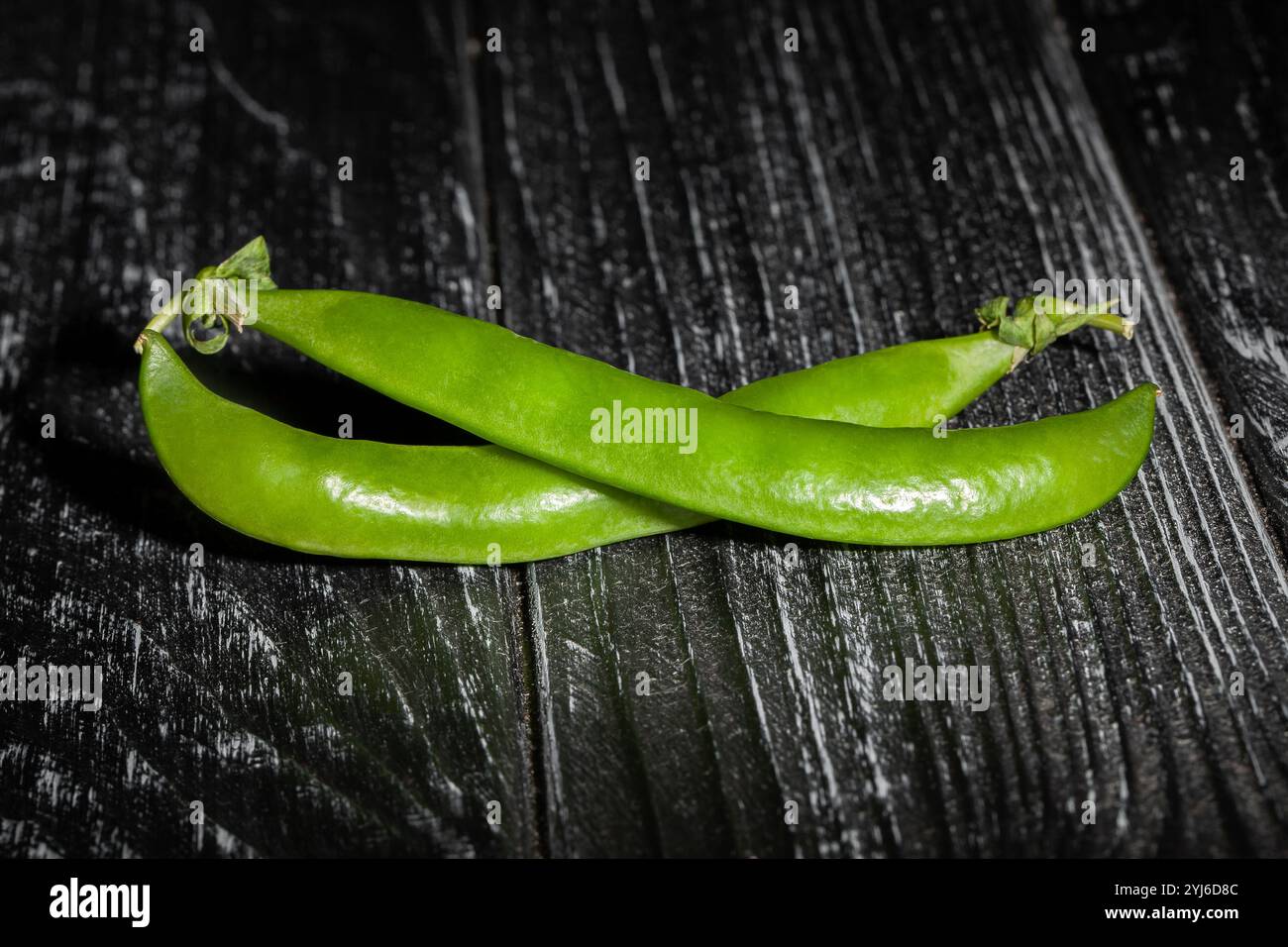piselli verdi su sfondo in legno nero Foto Stock